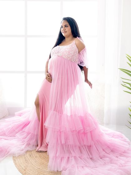 A beautiful shot of a mom-to-be in a pink layered gown, showcasing its length and flow in a bright, naturally lit studio.