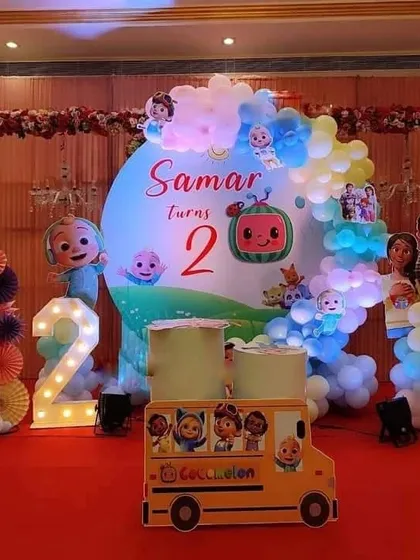 A vibrant Cocomelon theme for a second birthday party. This setup features a large backdrop with Cocomelon characters, a school bus cutout, and a marquee number '2'.