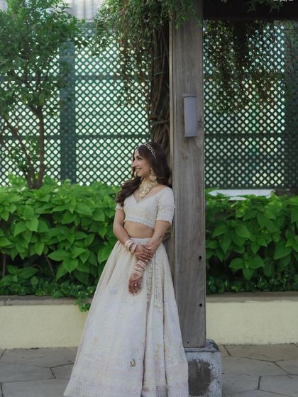 A full-length portrait of Sheena. Her soft golden hour makeup and ivory lehenga create a cohesive, elegant look that feels both traditional and contemporary.