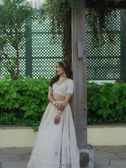 A full-length portrait of Sheena. Her soft golden hour makeup and ivory lehenga create a cohesive, elegant look that feels both traditional and contemporary.