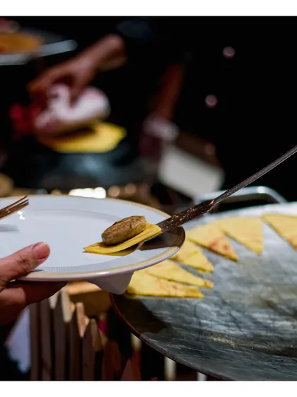 A freshly made gilauti kebab is carefully placed on a small, crisp bread base (bakarkhani). This close up shot emphasizes the delicate handling and perfect pairing of textures at our live tawa stations.