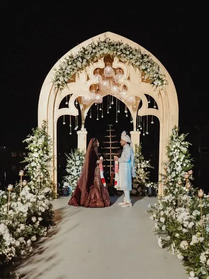The couple shares a quiet moment on the Varmaala platform we built over the lagoon. The elegant archway, adorned with white flowers and hanging glass globes, creates a romantic frame against the dark water and night sky.