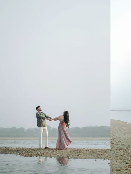 The couple holds hands, ready to twirl on a narrow strip of sand surrounded by water. The minimalist composition focuses entirely on their connection and the serene environment.
