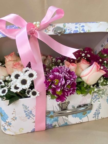 A charming floral suitcase for Mother's Day. This vintage-inspired trunk is filled with a beautiful assortment of pink and purple flowers, tied with a big pink bow.