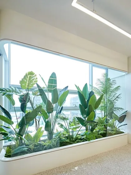 A large, built-in planter with a glass front in a modern office, filled with a variety of artificial plants. This creates a beautiful, self-contained garden view for the workspace.