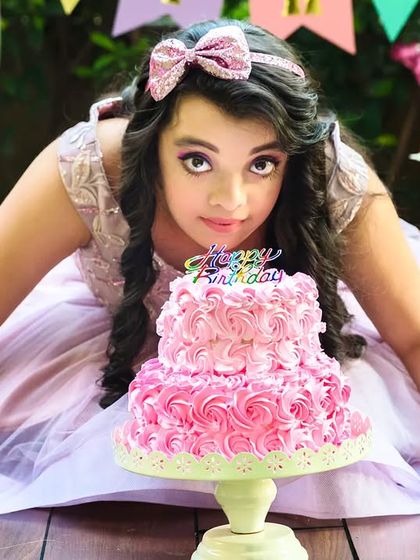 The birthday girl leans over her pink cake, ready to make a wish or take a bite, during her outdoor birthday celebration.