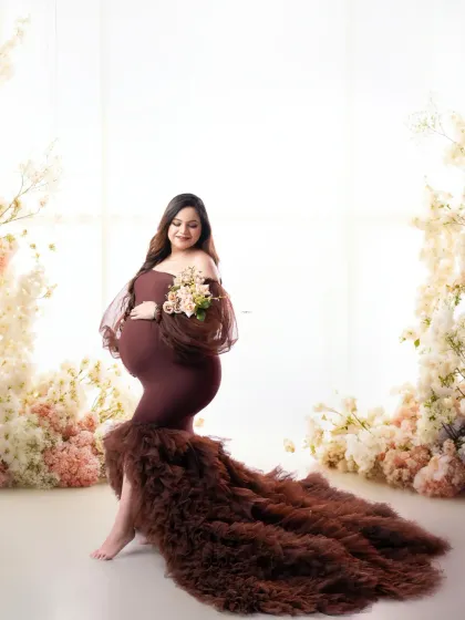 A beautiful portrait of the mother-to-be, with her partner's loving presence felt. The flowing brown gown and floral setting create a romantic, earthy feel.
