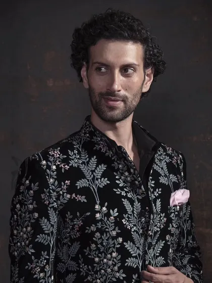 A close-up of the black floral embroidered jacket. The detail in the embroidery and the subtle pink pocket square highlight the artistry of the piece.