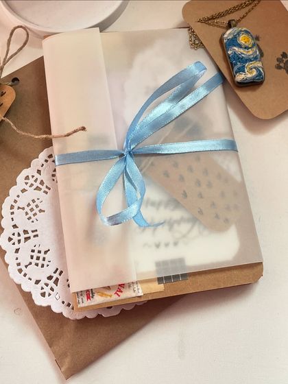 A peek at a complete gift package. It includes a custom card, a handmade necklace, and thoughtful wrapping with a ribbon and doily.