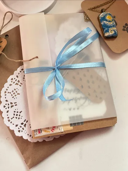 A peek at a complete gift package. It includes a custom card, a handmade necklace, and thoughtful wrapping with a ribbon and doily.