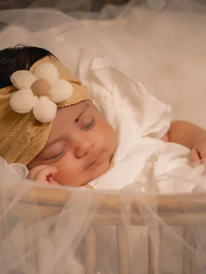 A peaceful portrait of a sleeping infant, adorned with a simple floral headband. I use soft, diffused light to gently illuminate the baby's features without disturbing their rest.