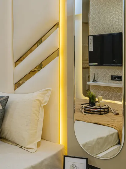 A close-up of the headboard design with white padding and gold accents. The warm vertical light strip adds a soft glow, making the bed area feel extra cozy and luxurious.