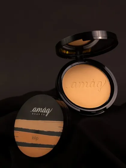 Set against a dark, draped fabric, this compact powder and puff create a sophisticated, moody scene. The lighting is focused to highlight the smooth texture of the powder and the elegant branding.