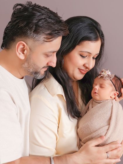 A classic portrait of new parents admiring their sleeping baby. The soft, neutral tones and their gentle expressions create a feeling of peace and contentment.