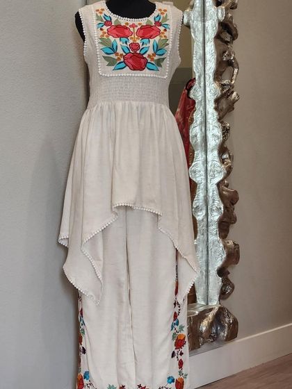 An artistic and chic fusion set. This outfit features an asymmetrical high-low top over pants, both adorned with colorful floral embroidery. It's a wearable work of art.