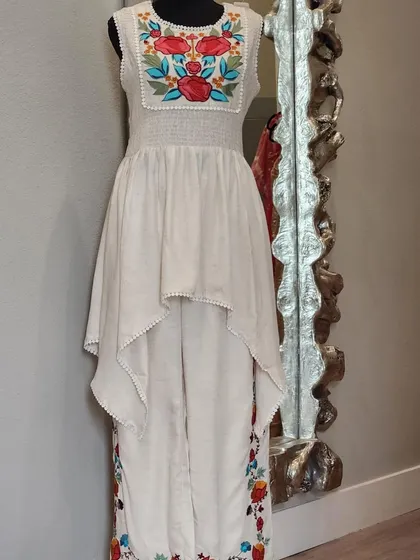 An artistic and chic fusion set. This outfit features an asymmetrical high-low top over pants, both adorned with colorful floral embroidery. It's a wearable work of art.