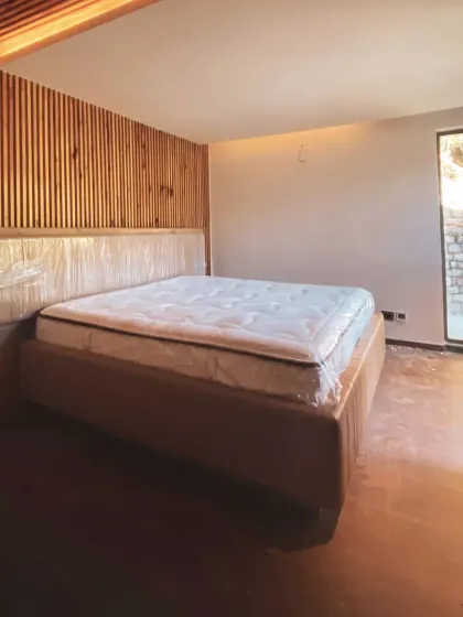 A bedroom in progress, featuring a slatted wood accent wall and a large window that frames the outdoor stone textures. This highlights our use of natural materials to create warm, modern interiors.