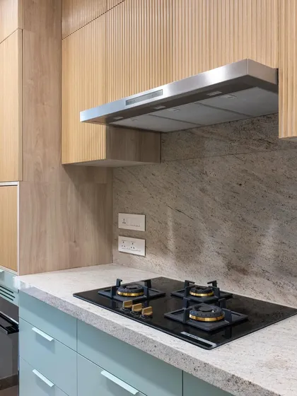 A close-up of the hob set against the quartz countertop and backsplash. The combination of the sleek black cooktop, the natural stone pattern, and the textured wood creates a rich sensory experience.