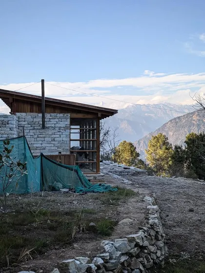 A quiet moment at our Uttarakhand site, with the snow-capped Himalayan range in the distance. The building's form, with its simple stone chimney and sloping roof, is a direct response to the climate and the traditional architecture of the region.