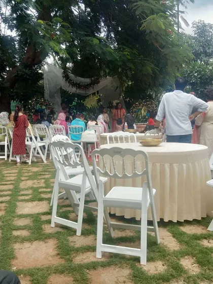 We can cater anywhere, including beautiful outdoor garden parties. Here's a daytime event setup with elegant white seating amidst the greenery, showing our flexibility for any venue, big or small.