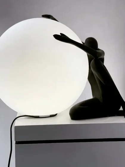 This art deco piece blurs the line between a table lamp and a sculpture. A stylized figure embraces a large, frosted glass ball, creating a comforting and intimate light source that is both artistic and deeply expressive.