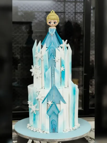 Let it go! This Frozen-themed cake brings Elsa's ice palace to life. The two-tiered design features a beautiful Elsa figurine atop her castle, which is constructed with geometric ice shards and decorated with delicate snowflakes. It’s a cool and elegant cake fit for a snow queen.