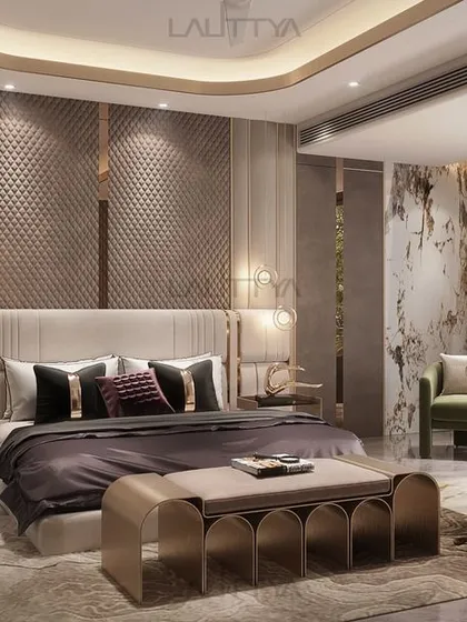 This luxurious modern bedroom features a plush, upholstered headboard with quilted detailing and chic pendant lights. The neutral tones with subtle gold accents create a warm and inviting atmosphere.
