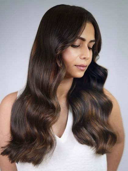 This look features warm cinnamon tones woven through a dark brunette base. The soft waves enhance the color's dimension, creating a glowing, radiant effect.