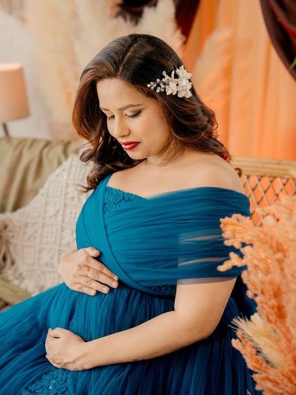 A close-up shot focusing on the serene expression of the mom-to-be. The details of the blue gown's bodice and the delicate hairpiece add a touch of elegance.