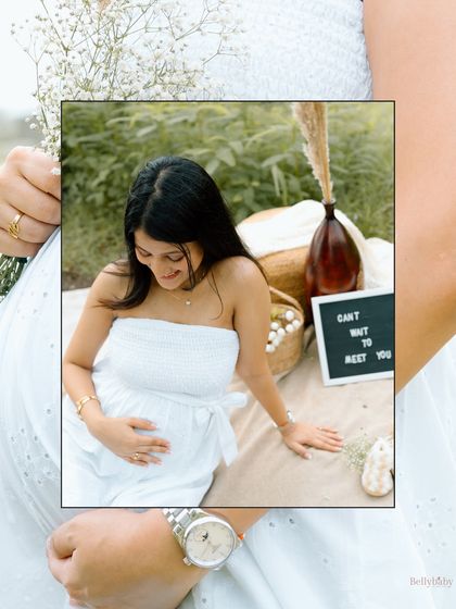 A creative, framed shot from a serene lakeside picnic. The focus is on her gentle expression as she cradles her bump.