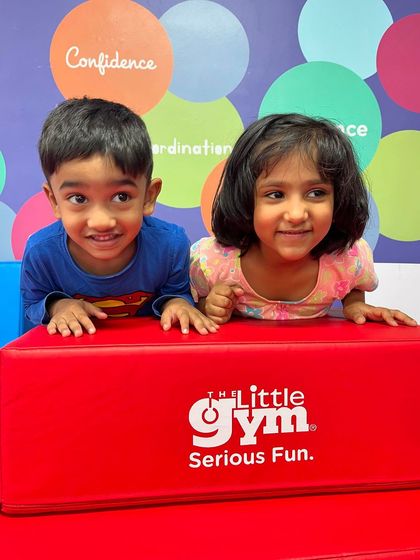 Two adorable friends peek over a soft block, sharing a happy moment. My gym is a place where friendships blossom and kids learn important social skills.