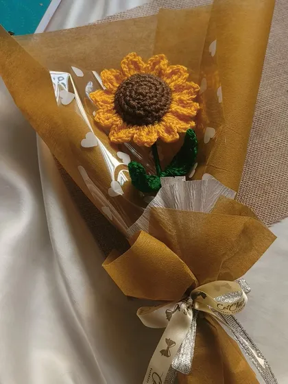A close up of a single wrapped sunflower. You can see the delicate cellophane with little hearts and the branded ribbon we use to tie it all together.