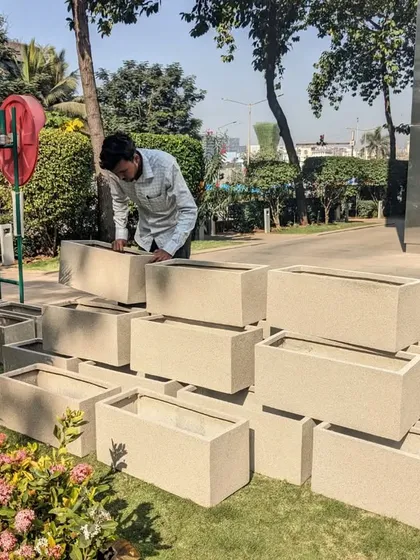 I am inspecting a stack of our light-colored, stone-textured FRP planters before installation. Their lightweight nature makes them easy to arrange and position on-site, even in large quantities.