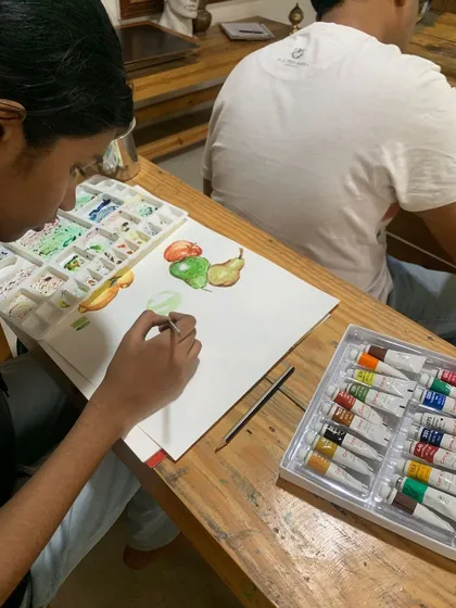 Another angle of students exploring the art of watercolor with still life. You can see the tube paints and palette, essential tools for any watercolor artist.