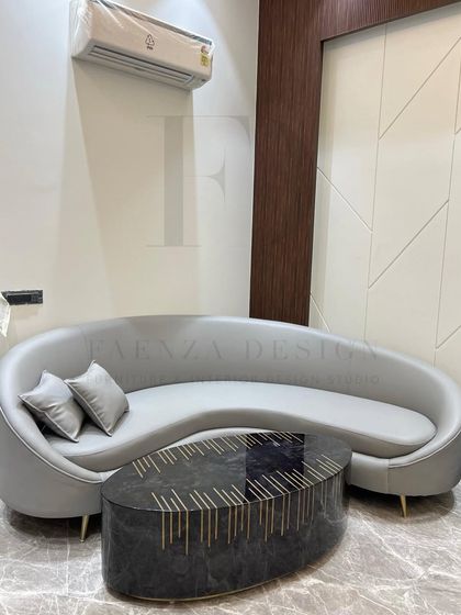 The gentle curve of this grey leather sofa adds a soft, organic feel to the room. It is perfectly paired with an oval-shaped coffee table featuring a black marble top and intricate brass inlay.