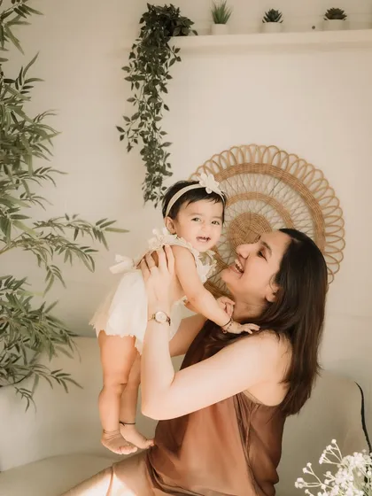 A mother lifting her daughter up, both sharing a beautiful, happy smile.