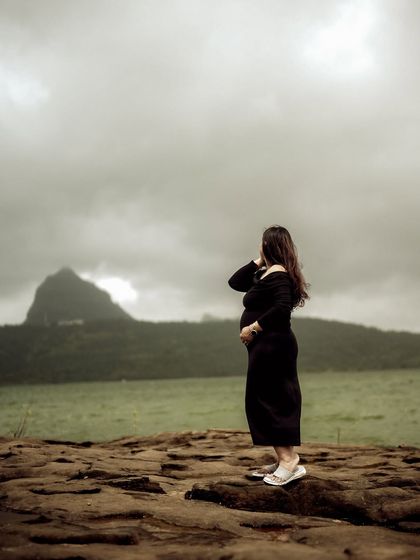 A powerful wide shot of the mom-to-be standing on a rocky outcrop, looking towards the mountains. It’s a portrait of strength and solitude on her motherhood journey.