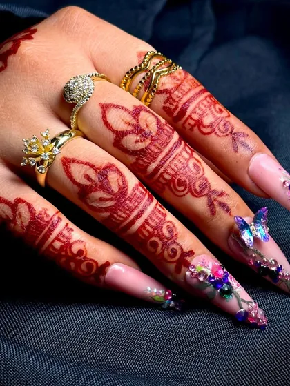 A beautiful fusion of traditions: intricate henna designs on the fingers paired with modern, embellished nail extensions.