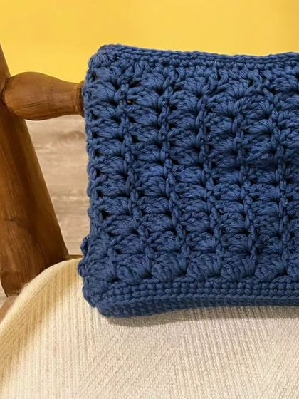 My upcycled clutch, resting on a chair. The rich blue color and textured stitch make it a beautiful statement piece for any outfit.