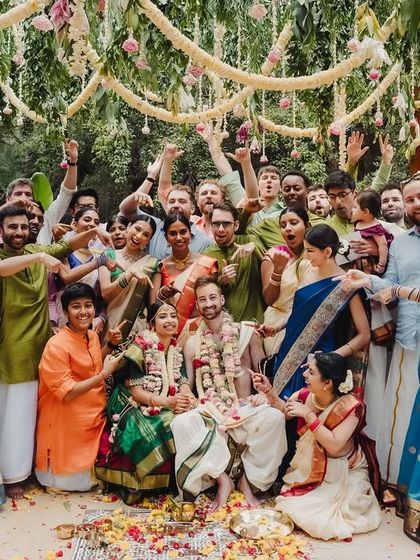 A large, happy group photo of guests from two different cultures celebrating together at the mandap.