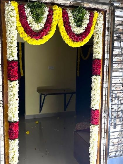 A home door decorated with garlands of red, yellow, and white flowers for a housewarming ceremony. This traditional design adds a festive touch.