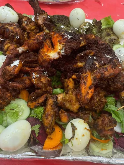 A close-up of one of my party platters, loaded with different styles of chicken starters, including tandoori legs, masaledar kebabs, and boiled eggs, all served on a fresh bed of salad.