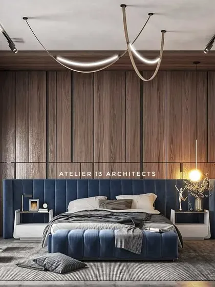 A bedroom design that makes a statement with a deep blue upholstered bed and a full-height wood-paneled wall. The custom lighting fixture adds a sculptural element, while large windows provide ample natural light.
