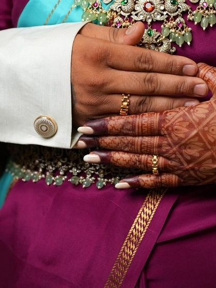 A close-up shot focusing on the couple's hands and rings during their engagement. The bride's mehendi, with its classic check pattern, adds to the beauty of the moment.