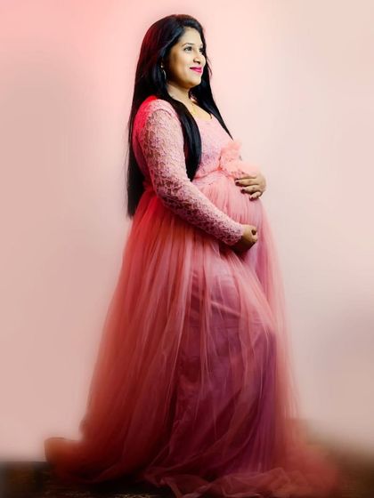 A classic side-profile maternity portrait. The pink lace-sleeve gown elegantly drapes over the baby bump, creating a timeless and beautiful silhouette.