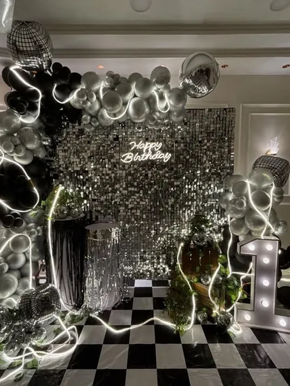 I create stunning, Insta-worthy backdrops that become the highlight of your party. This glam disco theme for a 13th birthday features a silver shimmer wall, a custom neon sign, a black and silver balloon arch with disco balls, and large marquee numbers.