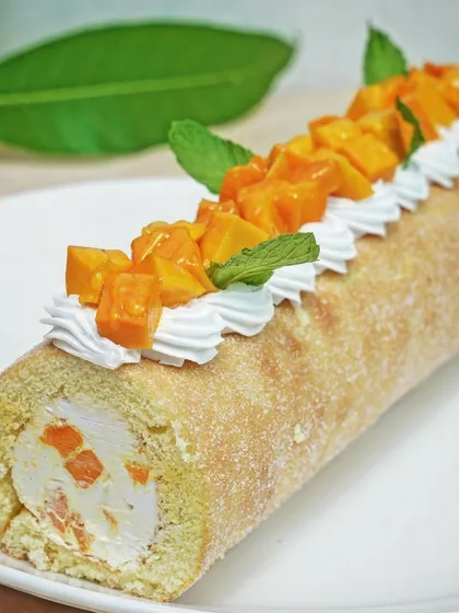 A beautifully presented mango cream swiss roll, topped with fresh mango chunks and mint. This image focuses on the elegant presentation of a specialty pastry item.