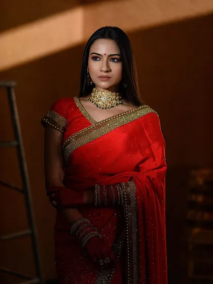 This shot uses dramatic side lighting to create depth and mood. The model in a red saree stands against a simple, warm-toned wall, showing how we use light to tell a story.