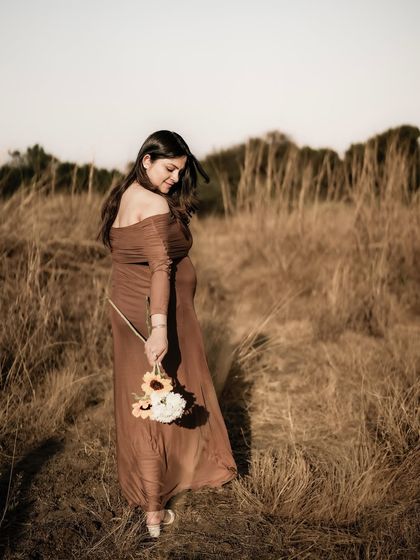 A beautiful shot of the mom-to-be walking through a golden field, looking down at her bouquet with a gentle expression.