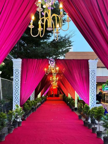 A bold and beautiful entrance tunnel created with vibrant magenta drapes. The chandeliers hanging within the walkway add a touch of glamour and light the way for an exciting celebration.